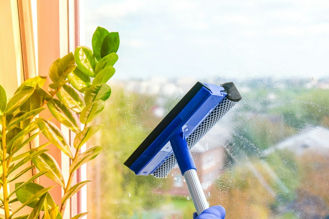 Employee hand in rubber protective glove cleans window with foam and puller. General spring cleaning